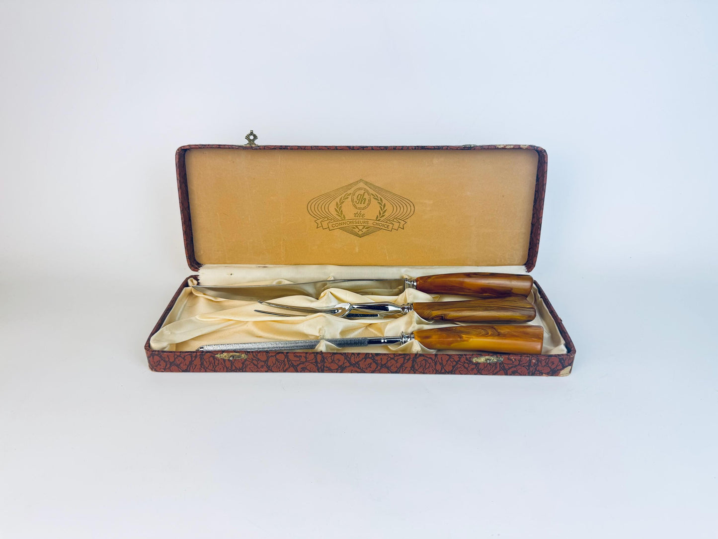 Vintage 1950s Glo-Hill carving set with butterscotch Bakelite handles displayed in original Connoisseurs Choice box lined with satin, showing carving knife, fork, and sharpening steel.