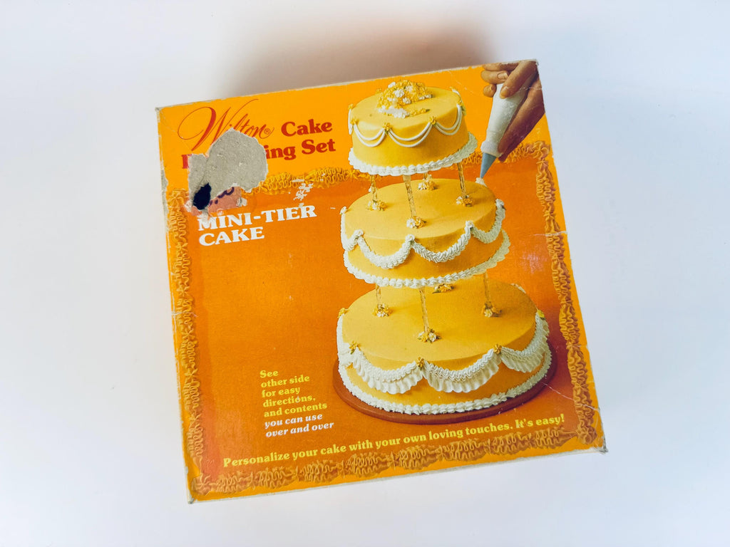 Vintage Wilton cake decorating set packaging with a tiered cake illustration on an orange background.