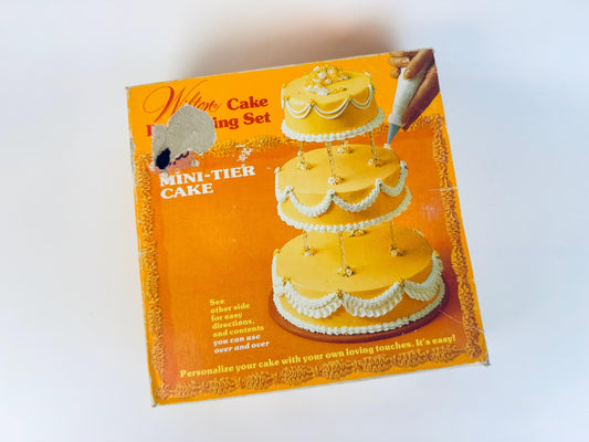Vintage Wilton cake decorating set packaging with a tiered cake illustration on an orange background.