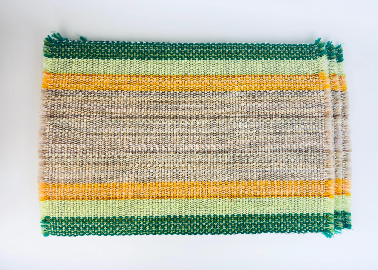 Woven mat with green, yellow, and beige stripes on a white background