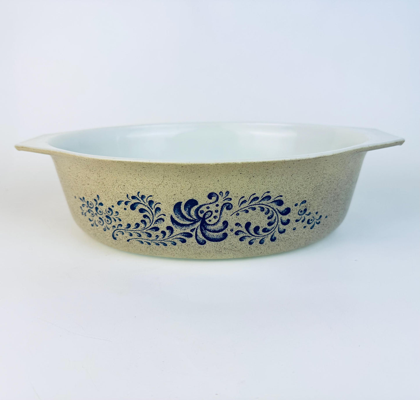 Vintage CorningWare casserole dish featuring the Blue Homestead pattern, with a speckled beige exterior and blue floral scroll design on white Pyroceram glass cookware.
