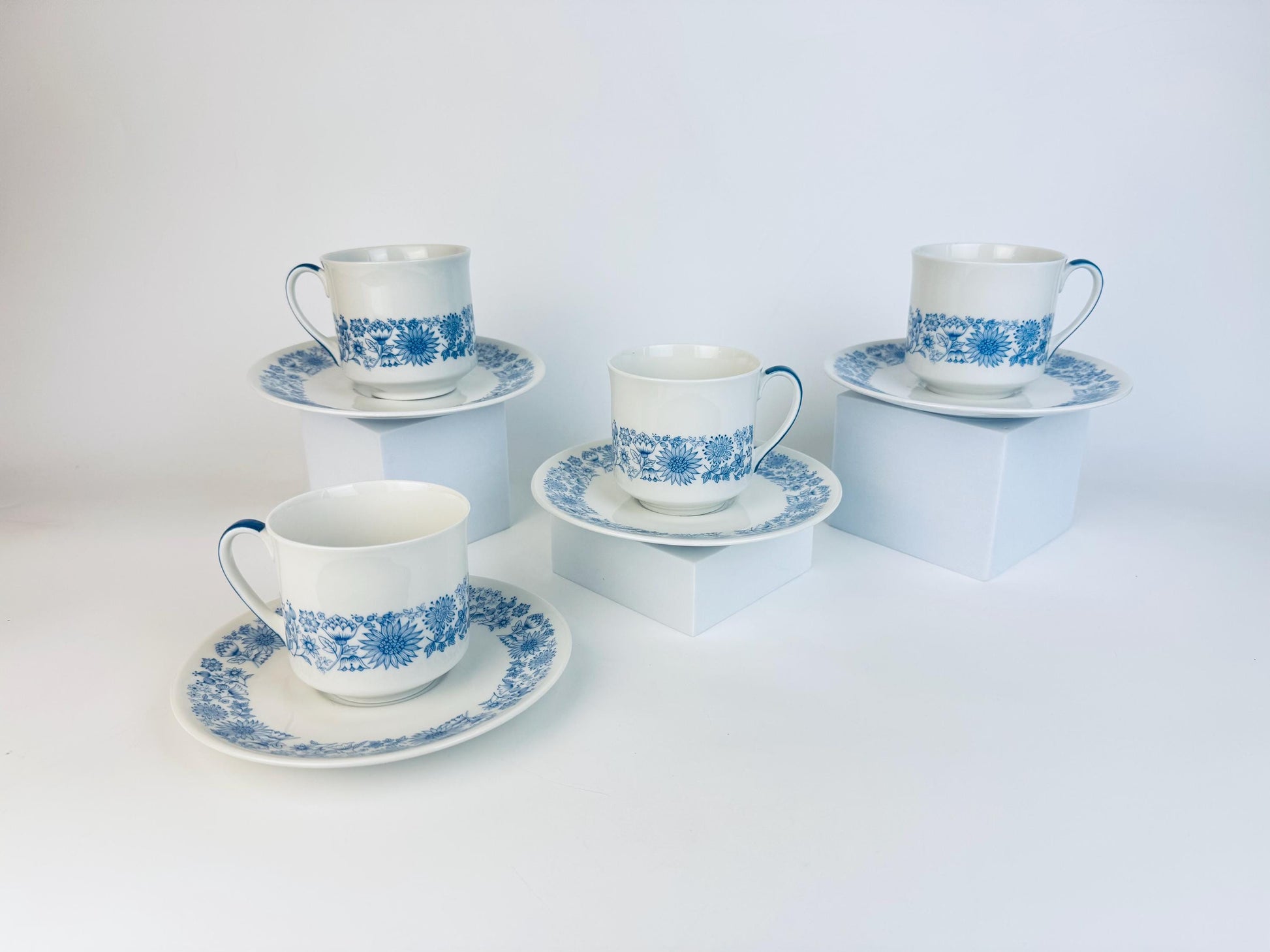 Set of four blue and white ceramic teacups and saucers on a white background