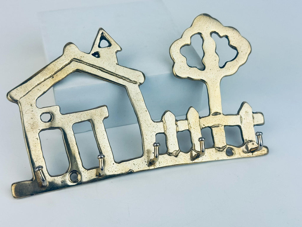 Decorative brass key holder shaped like a house and tree on a light blue background