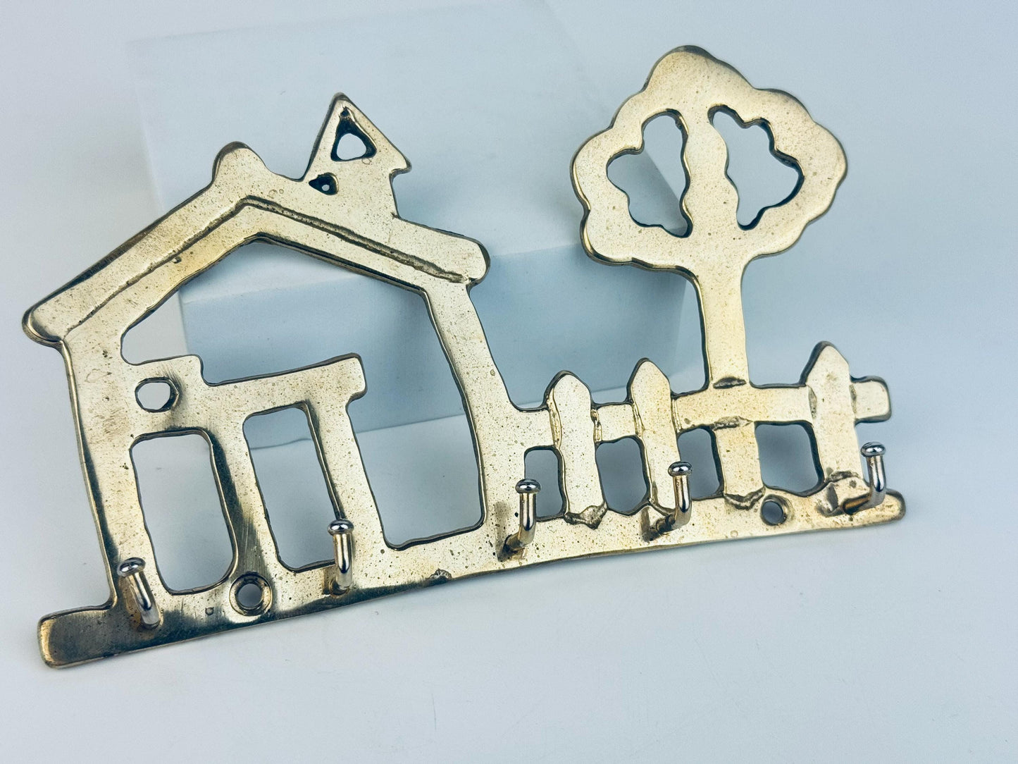 Decorative brass key holder shaped like a house and tree on a light blue background