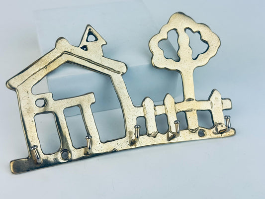 Decorative brass key holder shaped like a house and tree on a light blue background