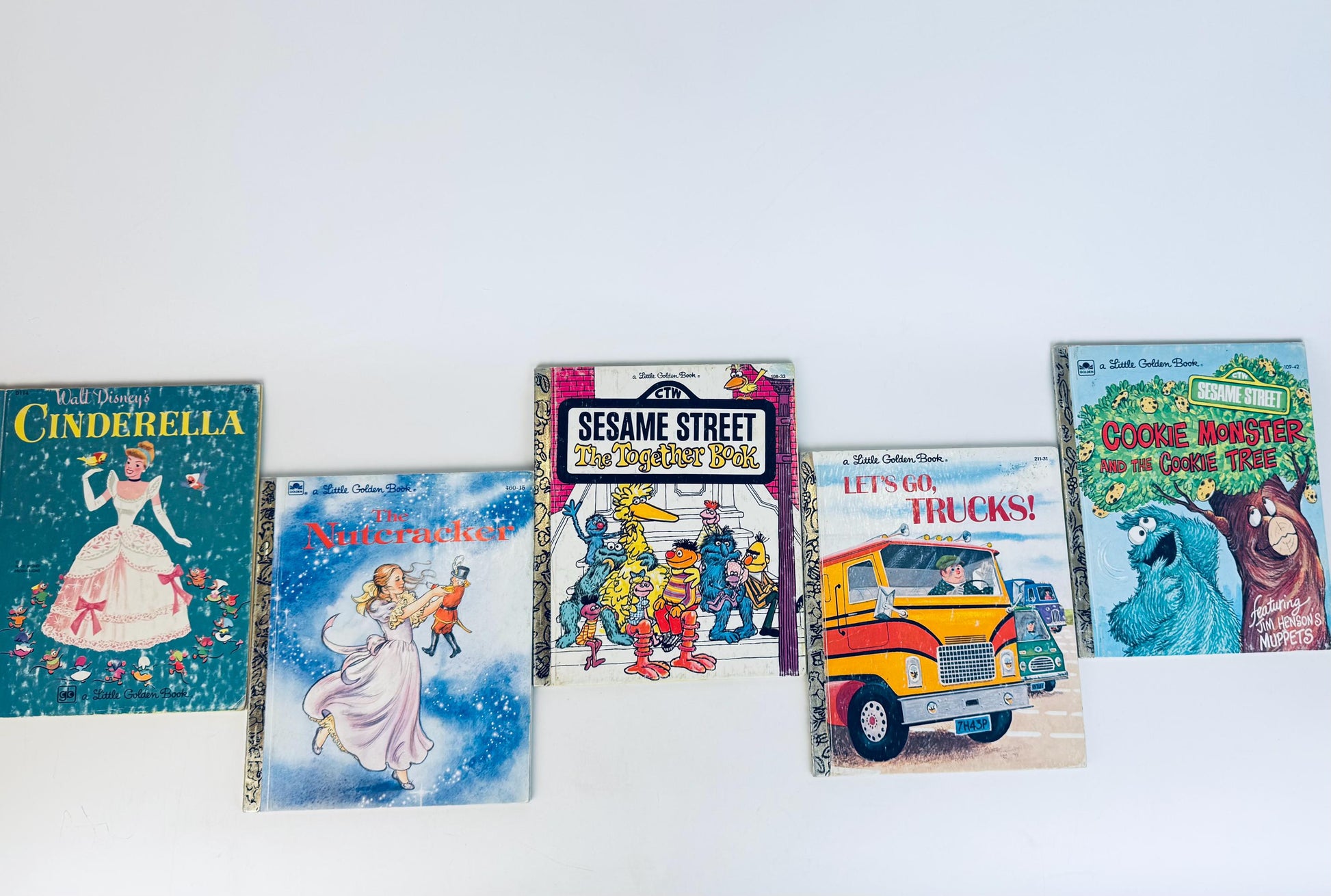 Five vintage Little Golden Books displayed in a row on a white background. Titles include Walt Disney’s Cinderella, The Nutcracker, Sesame Street: The Together Book, Let’s Go, Trucks!, and Sesame Street: Cookie Monster and the Cookie Tree. Each book features its original illustrated cover art in bright, nostalgic colours.