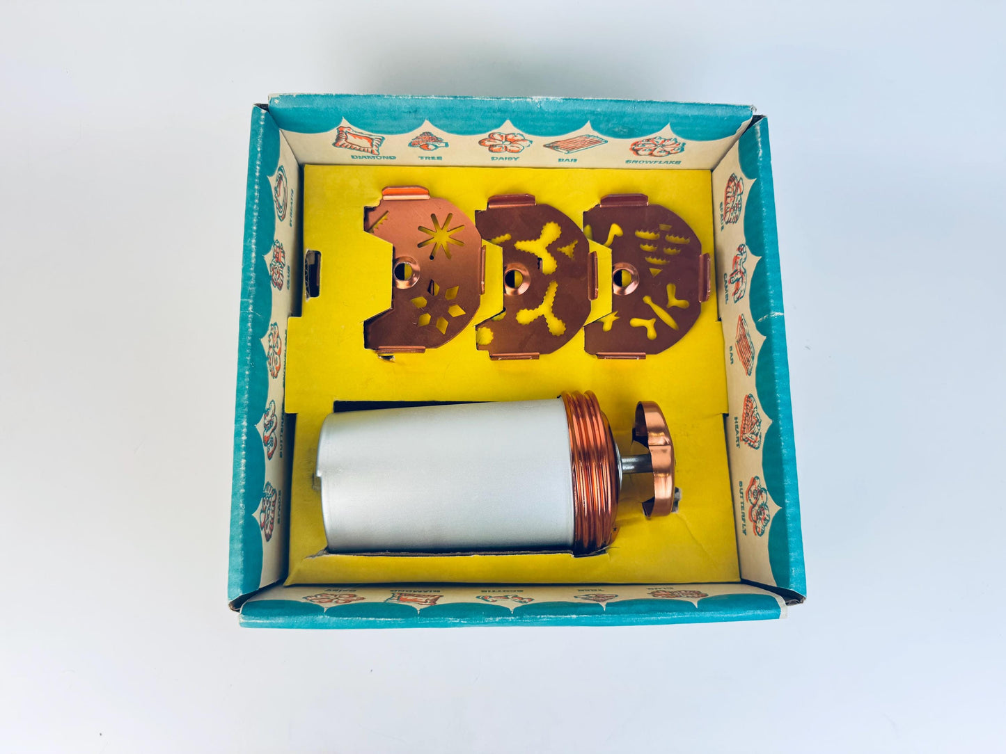 Mechanical cookie press components in a decorative box with a yellow interior