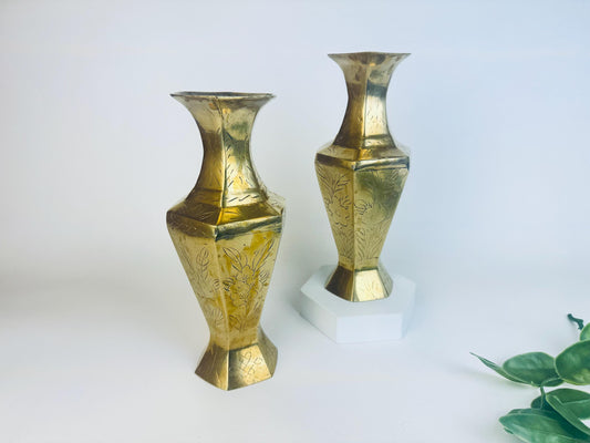 Two etched brass vases on a white background with a plant in the corner.