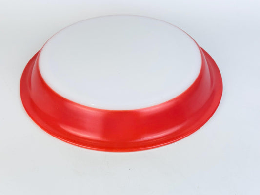 Underside view of a vintage Pyrex pie dish with a white centre and bright flamingo-pink rim, shown against a plain white background.