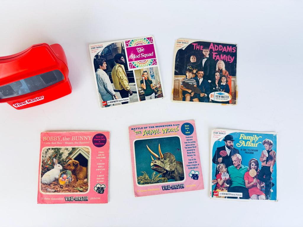 Five vintage 1960s View-Master reel sets displayed on a white background, including The Mod Squad, The Addams Family, Family Affair, Bobby the Bunny, and The Animal World, shown with a bright red View-Master viewer.