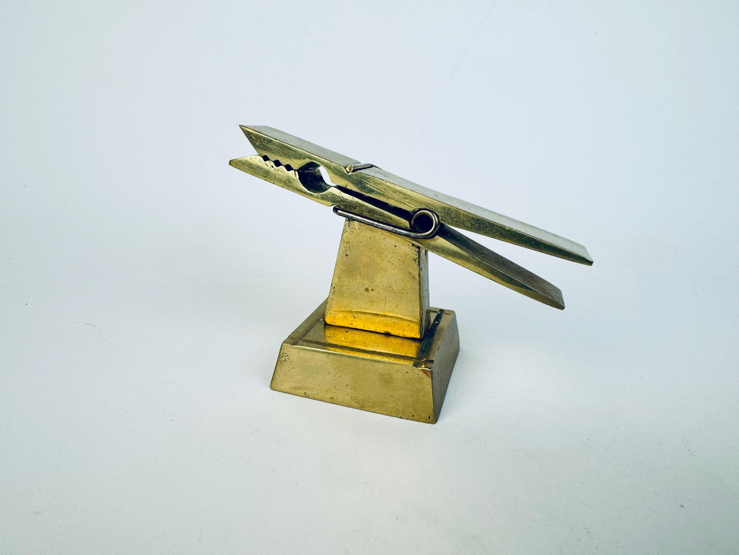 Vintage 1970s solid brass desk clip on a square pedestal base, shown angled to highlight its sculptural form and warm aged patina.