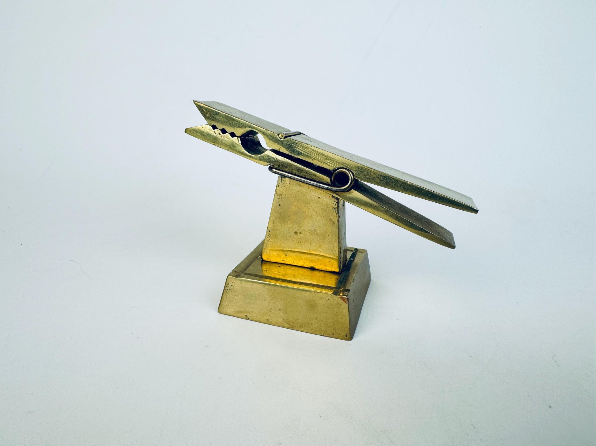 Vintage 1970s solid brass desk clip on a square pedestal base, shown angled to highlight its sculptural form and warm aged patina.