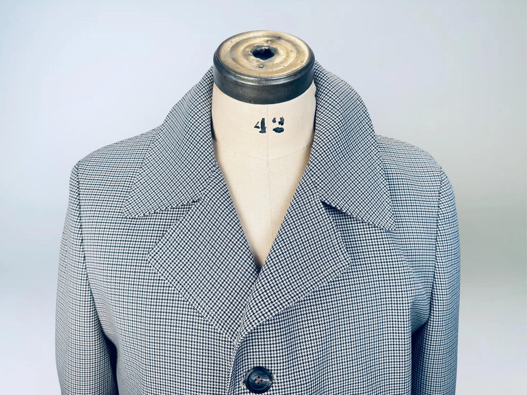Close-up of a vintage men’s trench coat displayed on a dress form, featuring a fine black-and-brown houndstooth pattern and wide notched lapel collar.