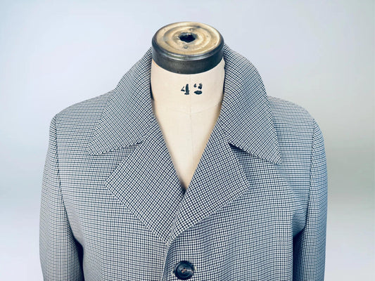 Close-up of a vintage men’s trench coat displayed on a dress form, featuring a fine black-and-brown houndstooth pattern and wide notched lapel collar.