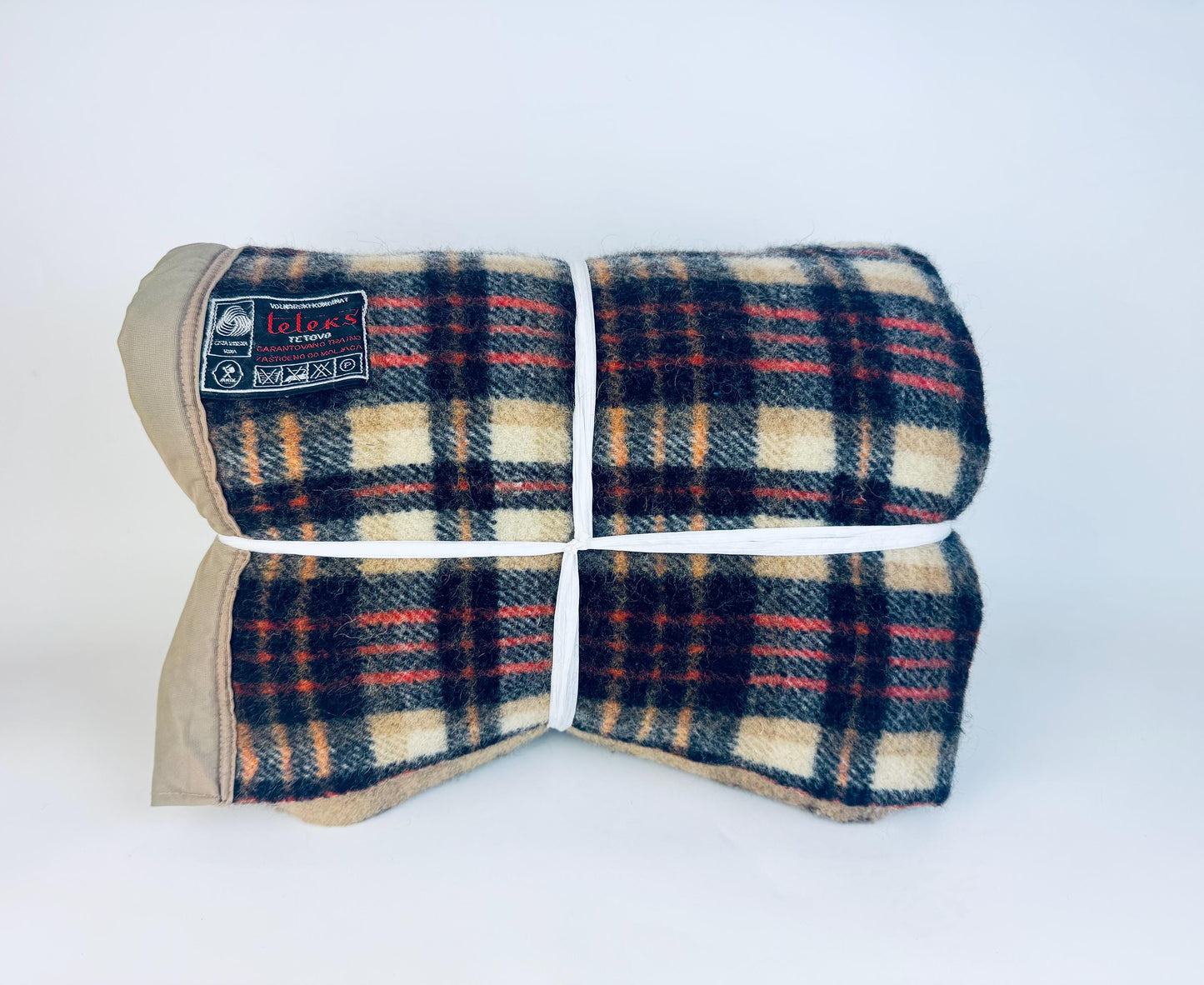 Folded vintage wool-blend Teleks Tetovo plaid blanket in tan, black, and rust tones, secured with white twine and showing the original woven label on the upper left corner.