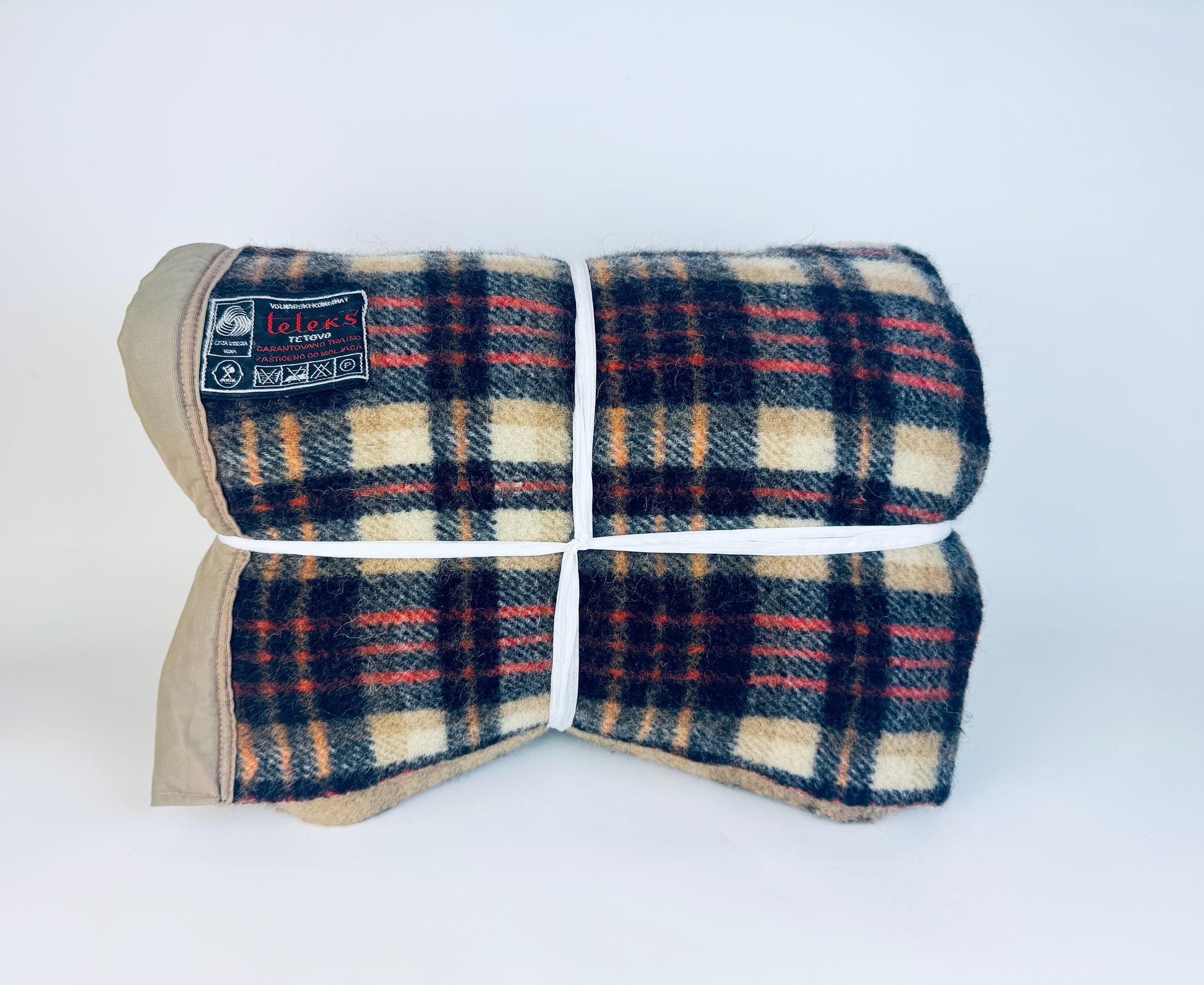 Folded vintage wool-blend Teleks Tetovo plaid blanket in tan, black, and rust tones, secured with white twine and showing the original woven label on the upper left corner.