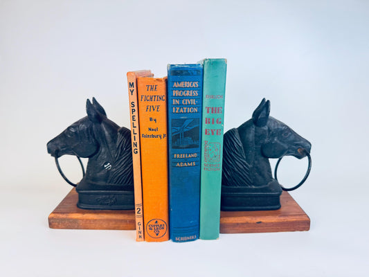 Pair of heavy Canada Forge cast-iron horse head bookends with ring detail on wooden bases styled beside vintage hardcover books.