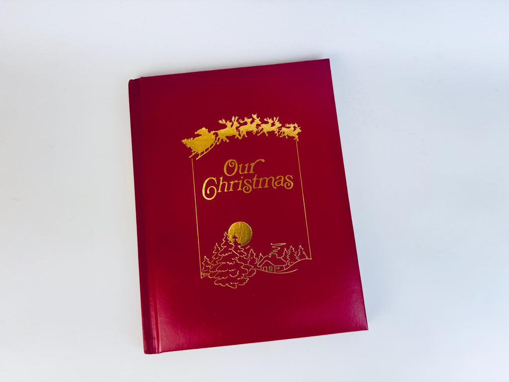 Vintage red leatherette hardcover book titled ‘Our Christmas’ with gold foil sleigh and reindeer illustration on the front cover.