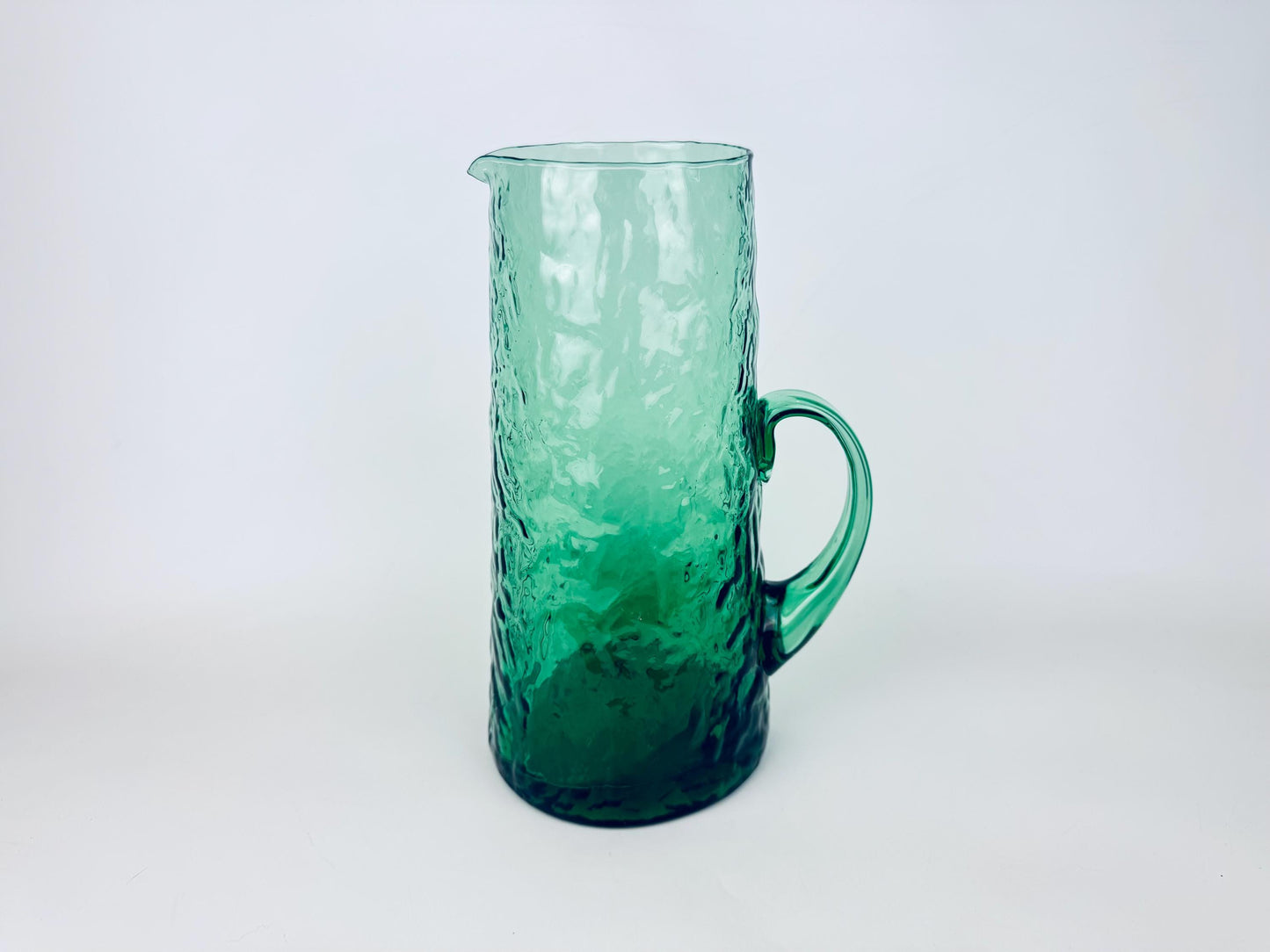 Tall vintage green textured glass pitcher with applied handle on white background.