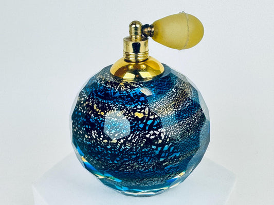 Vintage cobalt blue faceted crystal perfume atomiser bottle with gold hardware displayed on a white pedestal.