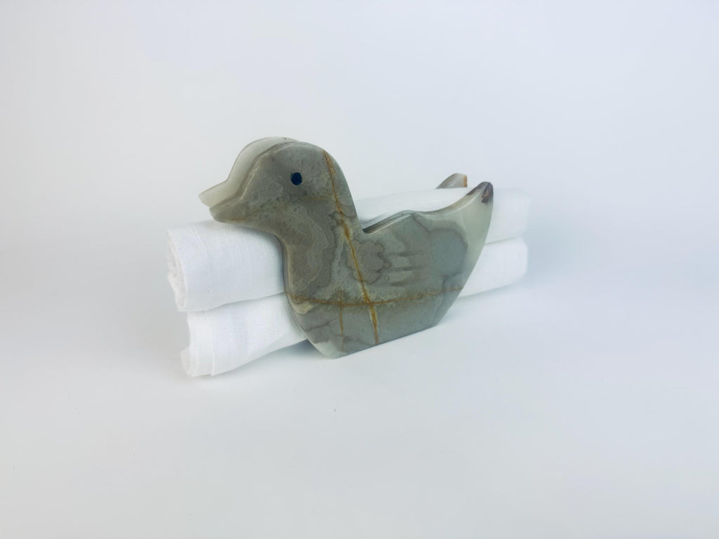 Grey stone duck-shaped onyx napkin holder displayed against a white background, shown holding neatly rolled white linen napkins.