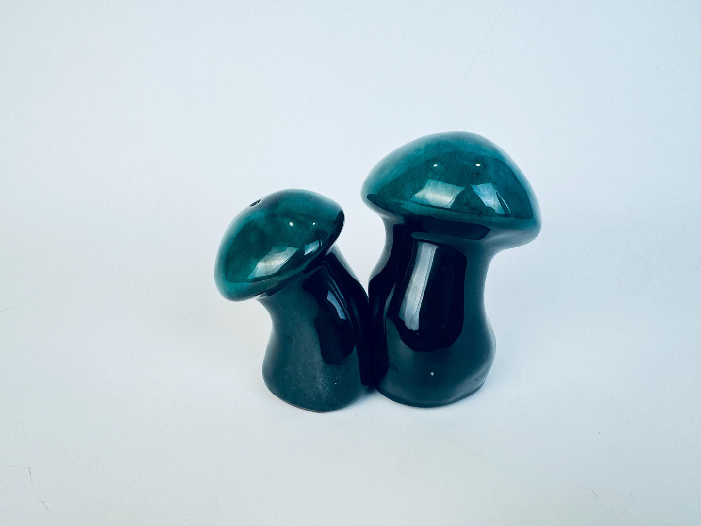 Two green ceramic mushroom shakers on a white background.