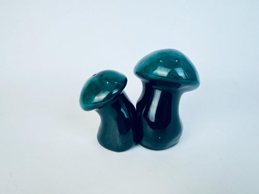 Two green ceramic mushroom shakers on a white background.