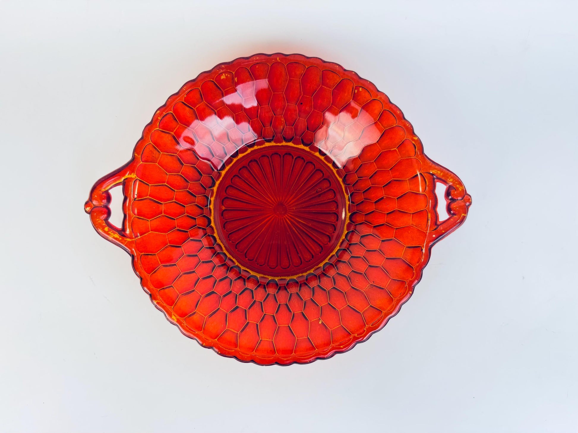 Vintage Amberina pressed-glass bowl with twin handles, featuring a honeycomb texture and radiant red-to-amber gradient, photographed from above against a white background.