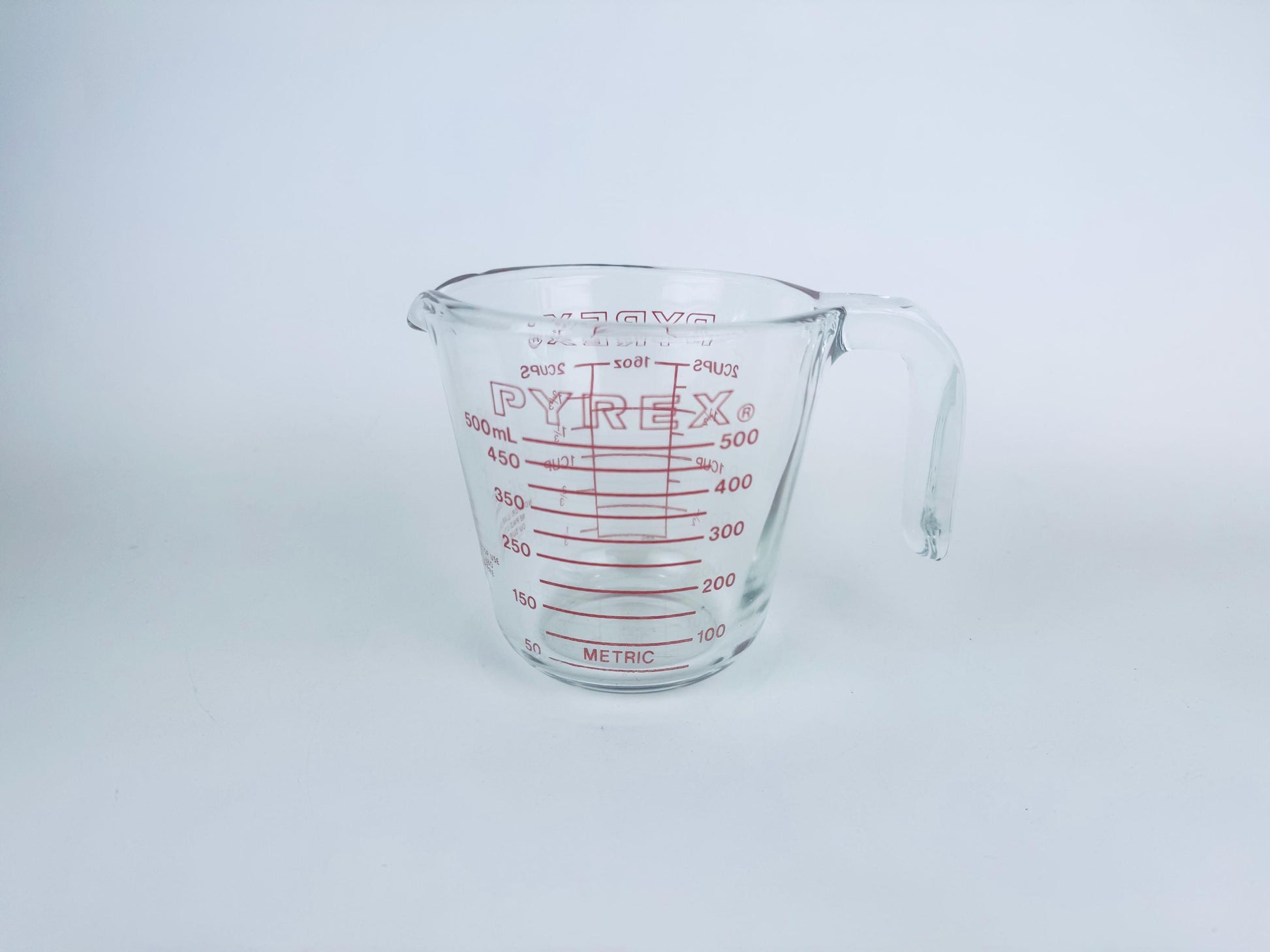 Vintage clear 2-cup Pyrex glass measuring cup with red metric and imperial markings, on white background.