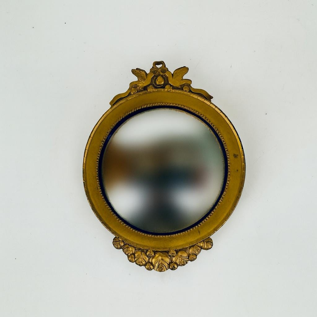 Close-up of a vintage brass convex mirror with beaded edge and sculpted dove crest.