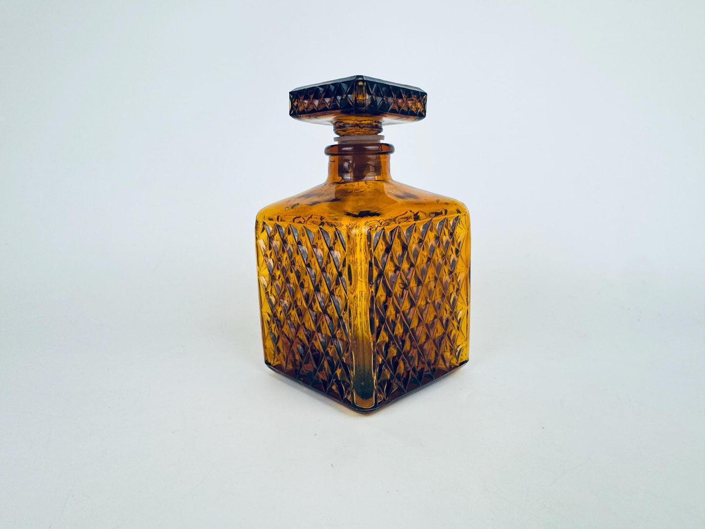Vintage amber glass decanter with a diamond-pressed pattern and square stopper, shown standing upright against a plain background.