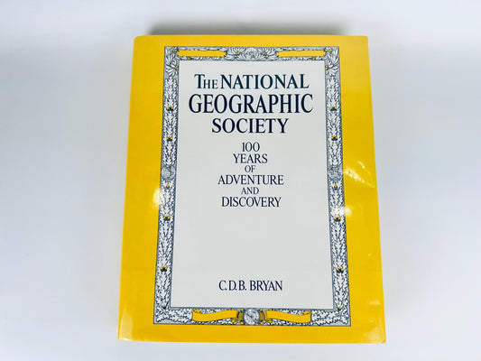 1987 vintage hardcover book ‘The National Geographic Society: 100 Years of Adventure and Discovery’ with bright yellow dust jacket displayed on white surface.
