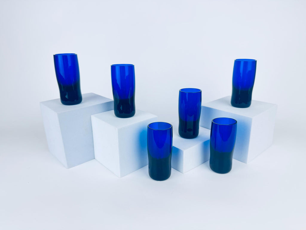Set of six vintage 1970s cobalt blue handblown glass shot glass with thick solid bases displayed on white blocks.