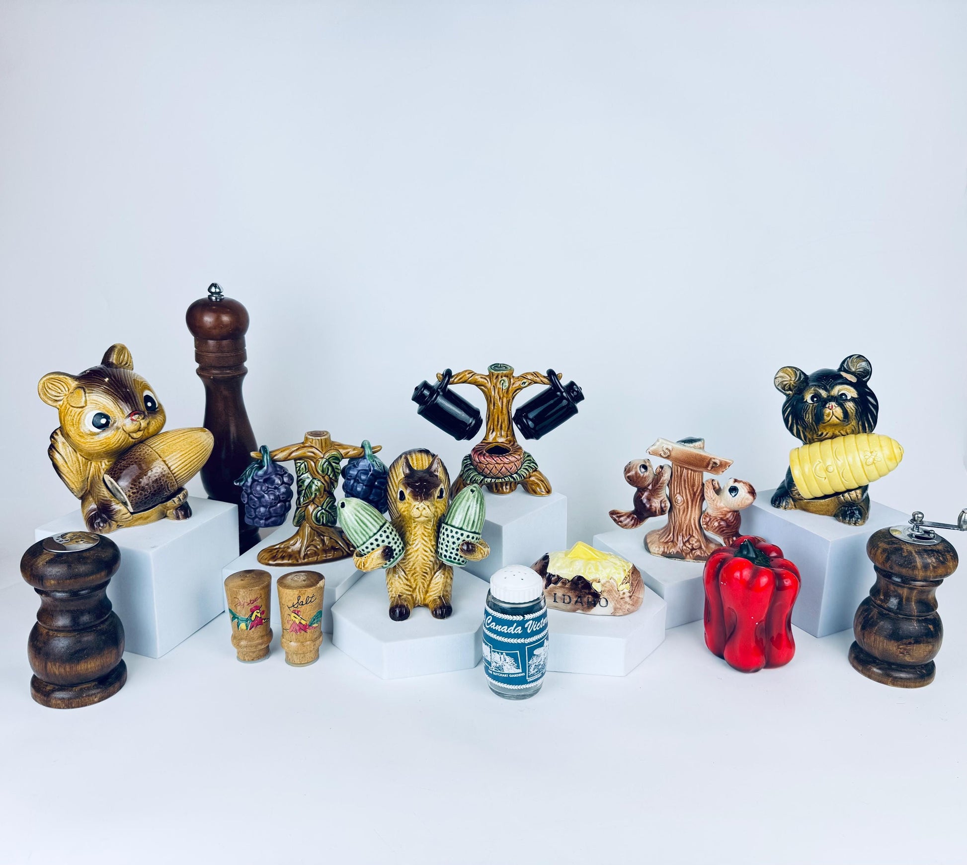 Vintage ceramic salt and pepper shaker sets featuring a brown squirrel holding an acorn and a black-faced bear holding a yellow pinecone, displayed on a white studio background among other retro collectibles.
