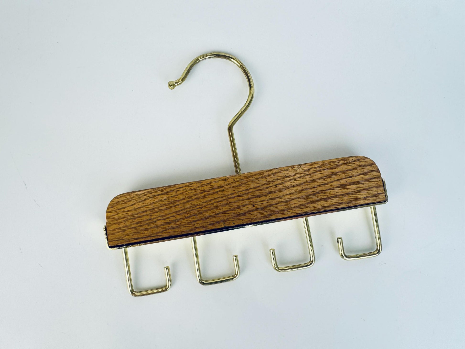 Vintage 1970s gold-tone metal and oak closet hanger with four hooks for belts, ties, or accessories, photographed on a white background.