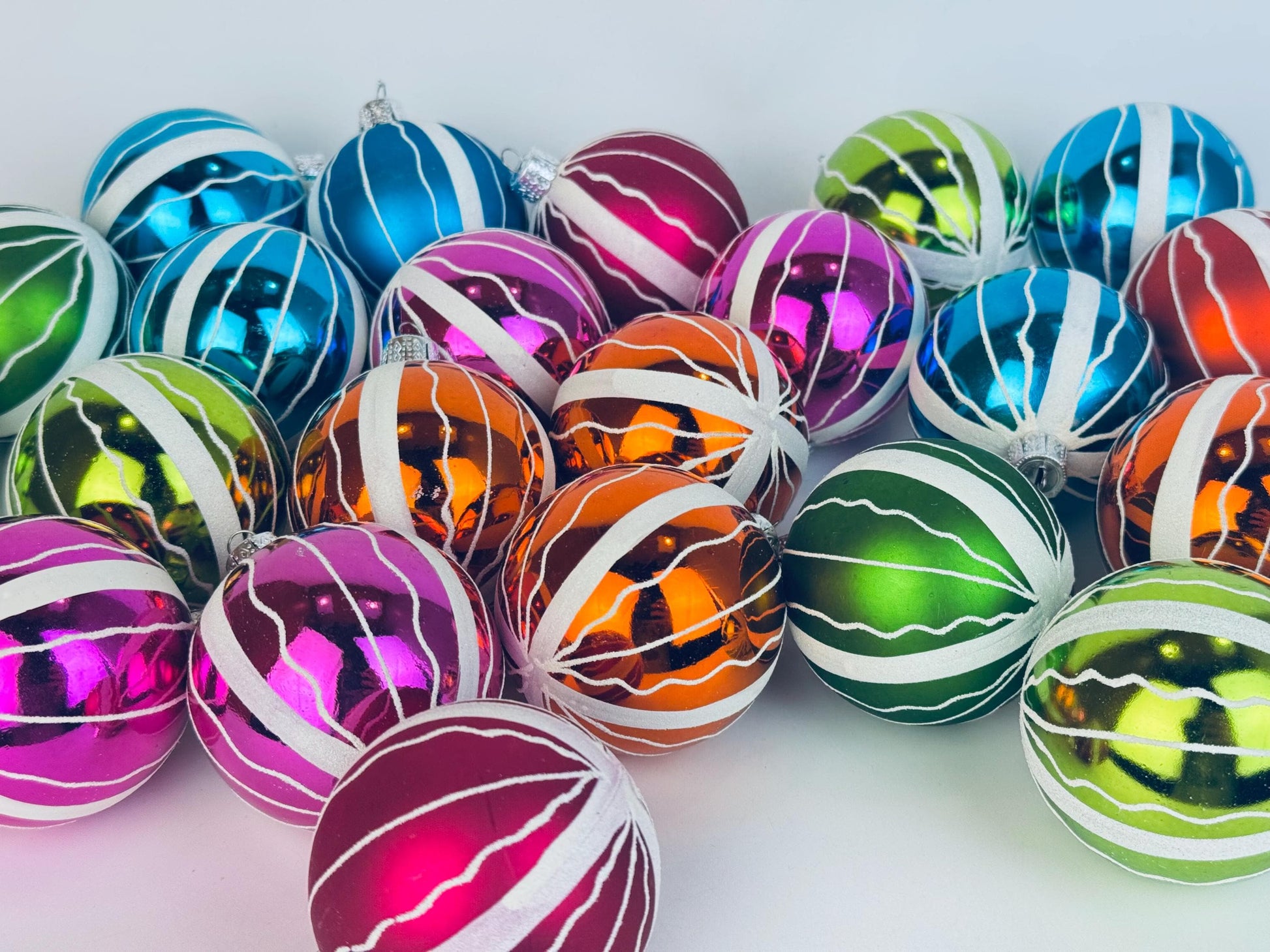 Assorted vintage 1970s hand-painted plastic Christmas ball ornaments in bright jewel-tone colours with white textured striping, arranged together against a clean white background.