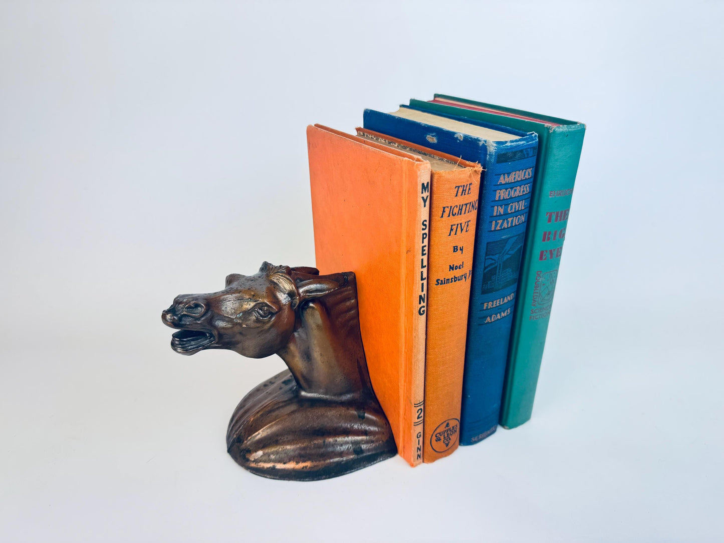 Vintage 1930s cast spelter horse-head bookend in bronzed finish, supporting a row of book spines.