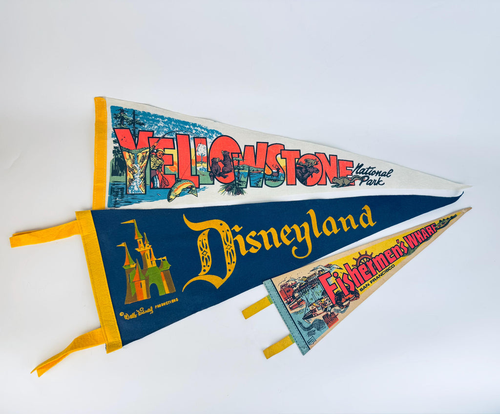 Three vintage mid-century felt souvenir pennants—Yellowstone National Park, Disneyland, and Fisherman’s Wharf—layered on a white background, each featuring bold retro graphics and colourful printed designs.