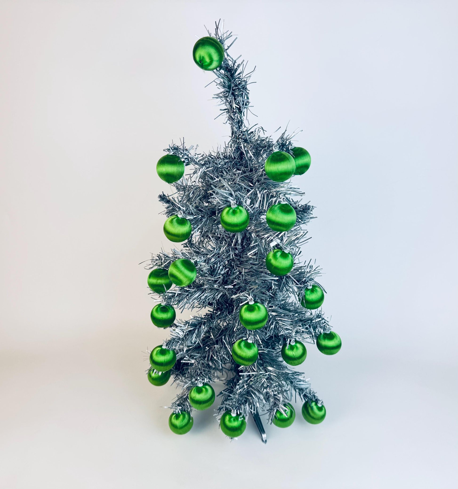 Vintage 1970s satin-thread green Christmas ball ornaments displayed on a silver tinsel tree, mid-century modern holiday décor.