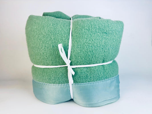 Folded vintage green wool blanket with light green satin border tied neatly with white cord.