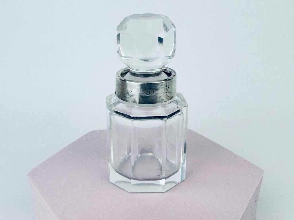 Close-up of early 1900s clear cut-glass perfume bottle with antique sterling silver collar and faceted stopper.