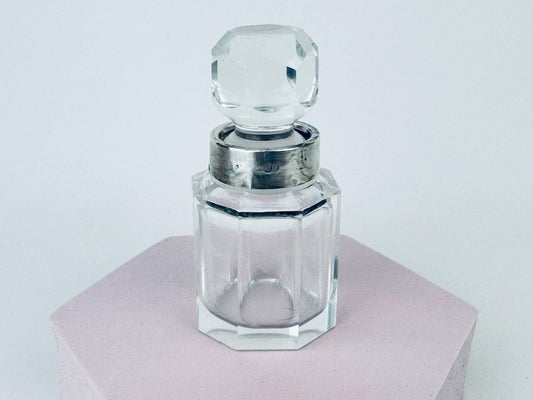 Close-up of early 1900s clear cut-glass perfume bottle with antique sterling silver collar and faceted stopper.