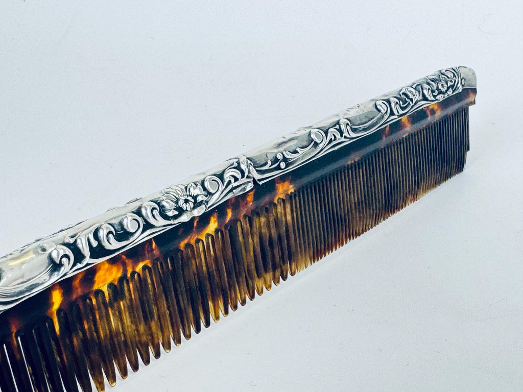 Vintage 1920s sterling silver comb with ornate repoussé scrollwork and amber faux-tortoiseshell celluloid insert displayed on a scale.