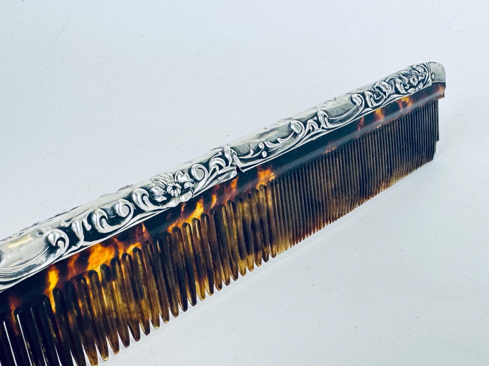 Vintage 1920s sterling silver comb with ornate repoussé scrollwork and amber faux-tortoiseshell celluloid insert displayed on a scale.