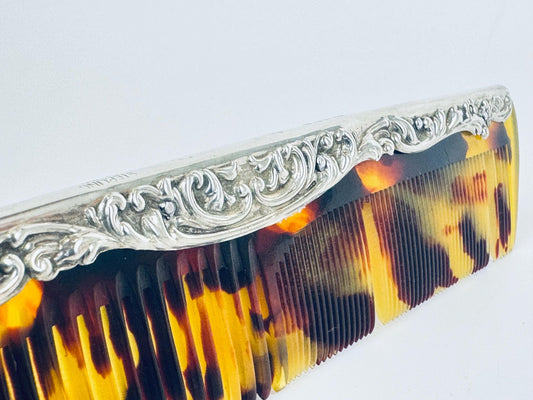 Vintage 1910s sterling silver comb with ornate repoussé scrollwork and amber faux-tortoiseshell celluloid insert displayed on a scale. 