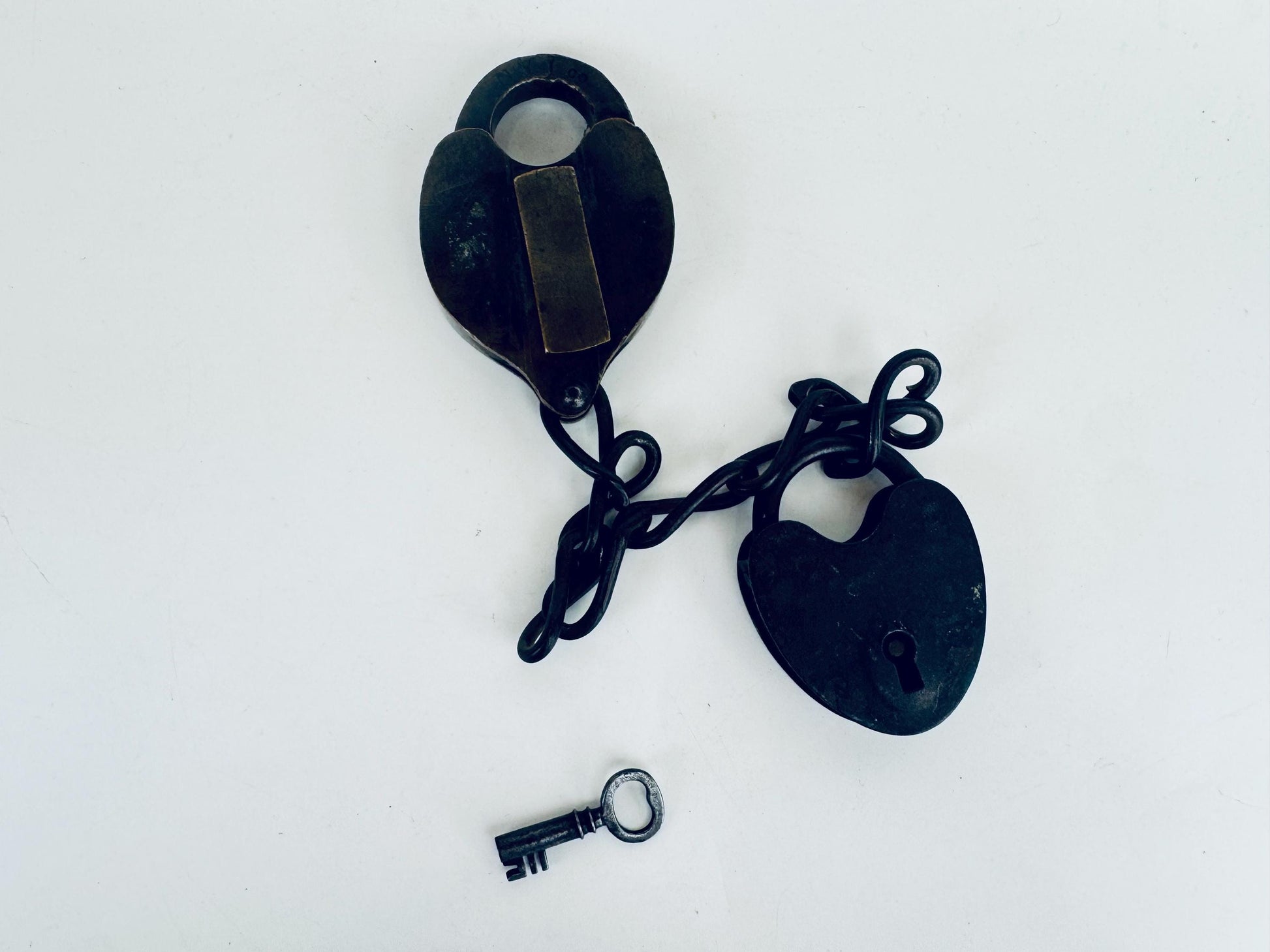 Close-up of a heavy, heart-shaped 1870s brass and iron railway padlock with original key inserted, showing patinated metal and worn keyhole, set on white background.