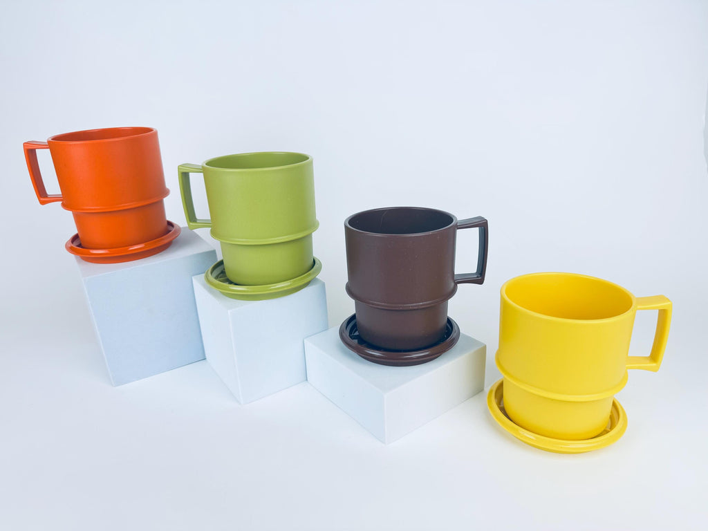 Four vintage 1970s Tupperware stackable mugs in orange, green, brown, and yellow, each shown with matching coaster-lids, arranged on white pedestals.