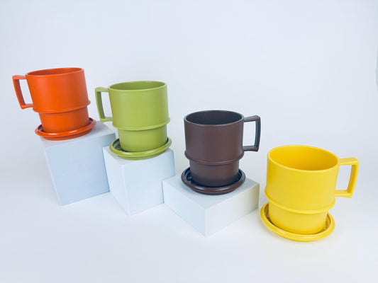 Four vintage 1970s Tupperware stackable mugs in orange, green, brown, and yellow, each shown with matching coaster-lids, arranged on white pedestals.
