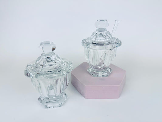 Two vintage Baccarat Bretagne clear crystal mustard pots with faceted lid and one with a matching spoon displayed on a pink hexagonal stand
