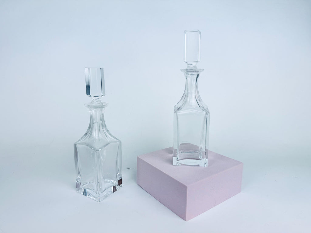 Pair of vintage Cartier clear crystal cruets with squared stoppers displayed against a red background, showing geometric form and light refraction.